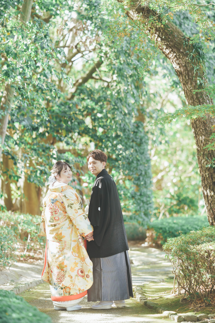 新郎と新婦が手を繋いでおり、庭園の道端でふたりとも振り向いている写真