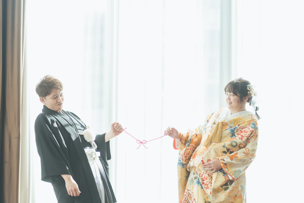 新郎と新婦が蝶々結びしている紐を引っ張り合って、新郎がすごい顔をしている写真