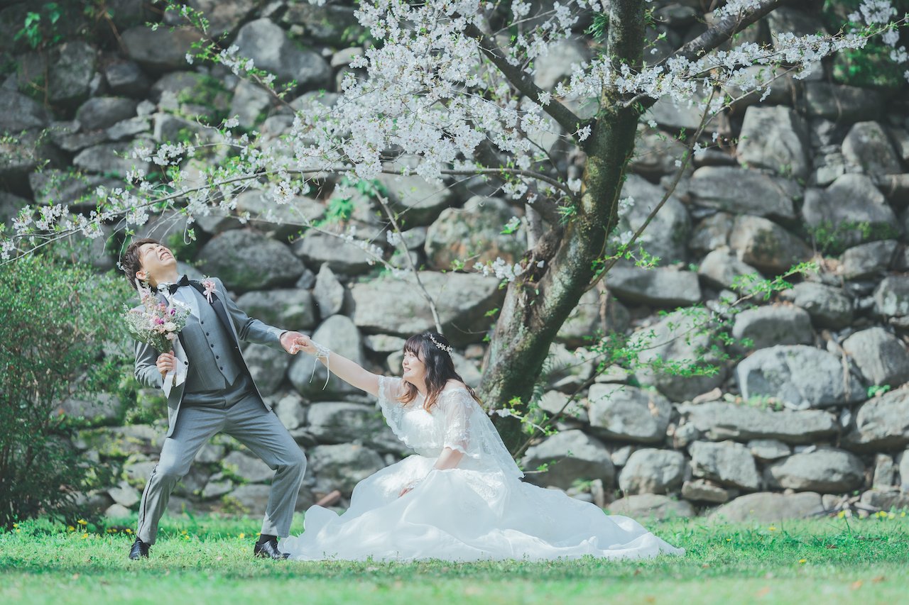 新郎が新婦を桜の下で引っ張って持ち上げようとしている写真