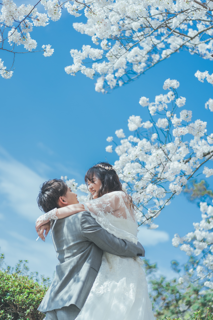 新郎が桜の下で新婦を抱きかかえて見つめ合っている写真